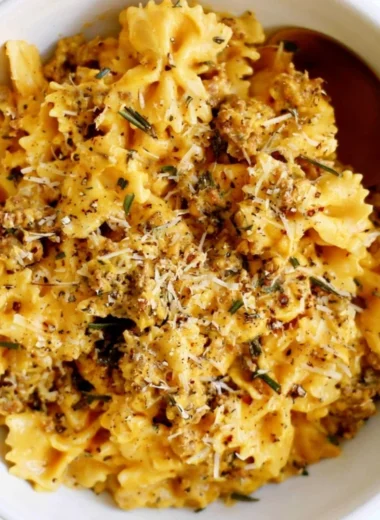 Creamy pumpkin pasta topped with herbs and cheese in a cozy setting.